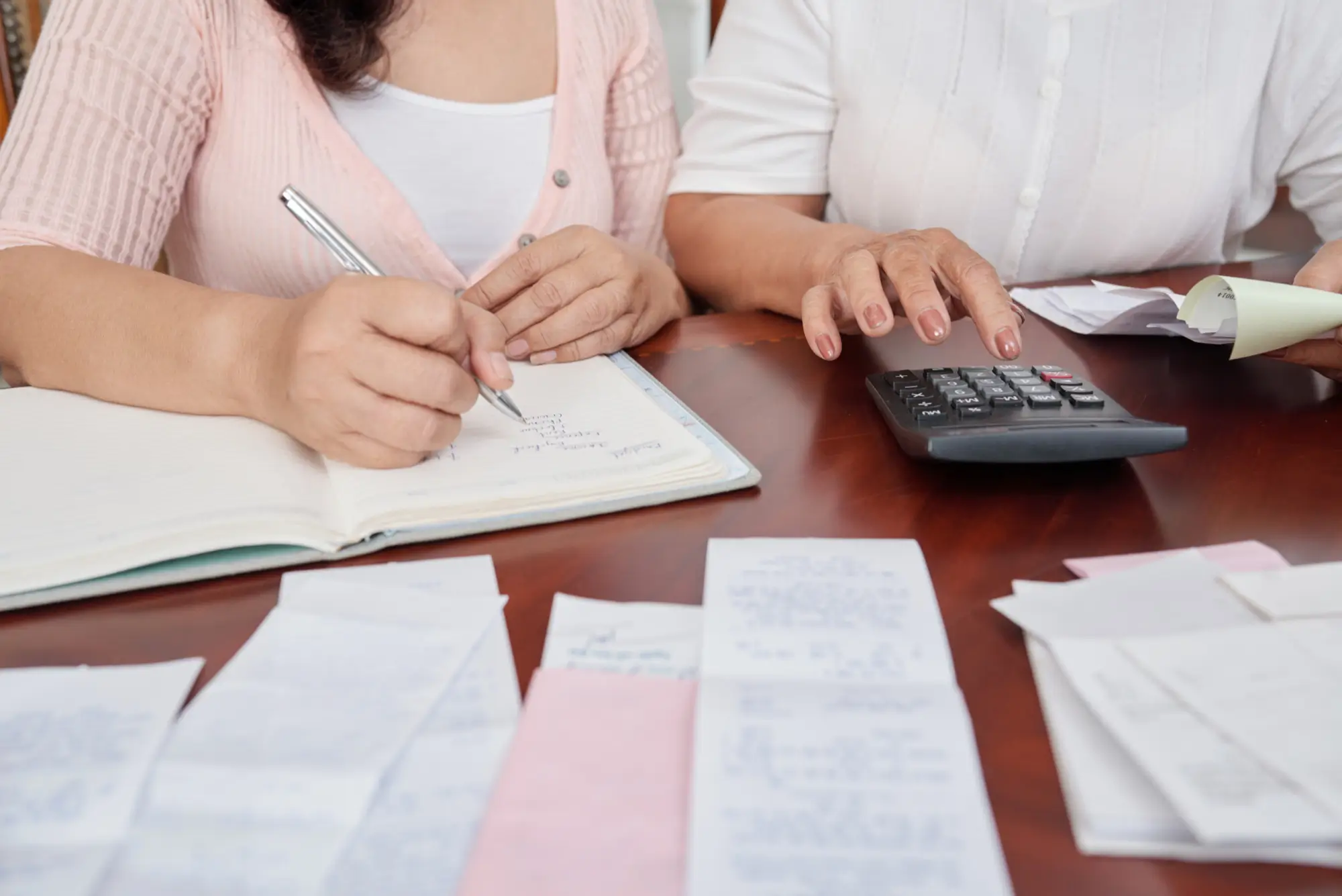 women sitting at table with receipts, counting on calculator